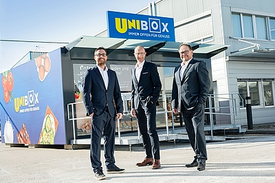 Drei Personen stehen vor neuer UNIBox