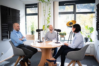 Drei Personen sitzen rund um einen Tisch. In der Mitte stehen Mikrofone. Foto: © BMLRT/Paul Gruber