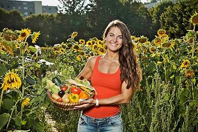 Person steht mit Gemüsekorb in einem Sonnenblumenfeld. © Morgentau